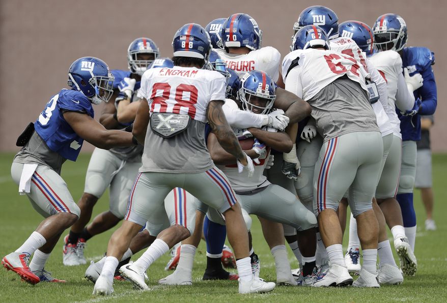 New York Giants running back Paul Perkins, center, is swarmed by teammates while running a play during NFL football training camp, Tuesday, Aug. 8, 2017, in East Rutherford, N.J. (AP Photo/Julio Cortez)