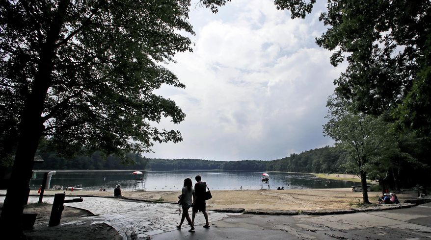 FILE - In this July 12, 2017 file photo, a couple walks along the shore of Walden Pond in Concord, Mass. Two centuries after Thoreau's birth, people are still following in Thoreau's footsteps to discover Walden Pond, the little lake he immortalized, and its picturesque and historic environs. (AP Photo/Charles Krupa, File)