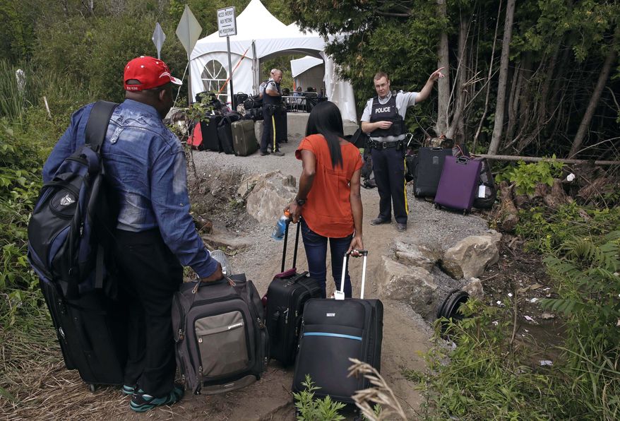 A Royal Canadian Mounted Police officer informs a migrant couple of the location of a legal border station, shortly before they illegally crossing from Champlain, N.Y., to Saint-Bernard-de-Lacolle, Quebec, Monday, Aug. 7, 2017. Officials on both sides of the border first began to notice last fall, around the time of the U.S. presidential election, that more people were crossing at Roxham Road. Since then the numbers have continued to climb. (AP Photo/Charles Krupa)