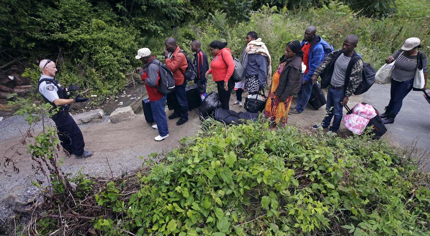 A Royal Canadian Mounted Police officer, left, standing in Saint-Bernard-de-Lacolle, Quebec, advises migrants that they are about to illegally cross from Champlain, N.Y., and will be arrested, Monday, Aug. 7, 2017. Officials on both sides of the border first began to notice last fall, around the time of the U.S. presidential election, that more people were crossing at Roxham Road. Since then the numbers have continued to climb. (AP Photo/Charles Krupa)