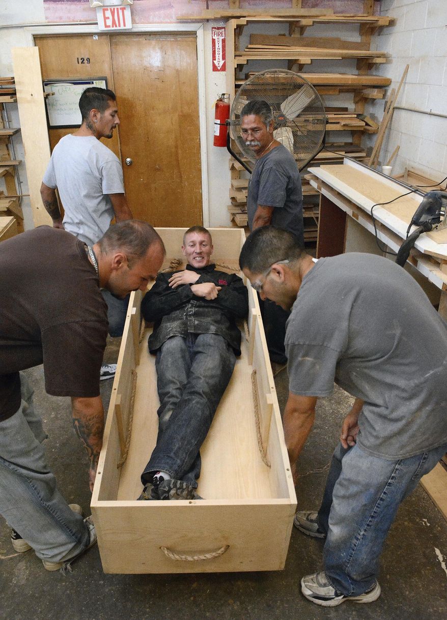This photo taken July 7, 2017, shows Alfredo Baca testing a Kosher casket as other members of the group pick it up and listen for sounds that might alarm them that it is not built right. They have led lives eroded by addictions, violence and prison, but with all that behind them, the men working in the wood shop at Fathers Building Futures in in Albuquerque, New Mexico, are reconstructing their own lives while building something reverential. The men, all of them fathers, have been trained to build kosher caskets used by members of the Jewish community – although the simple wooden construction has grabbed the attention of others who are interested in them as a final resting receptacle. (Jim Thompson/The Albuquerque Journal via AP)