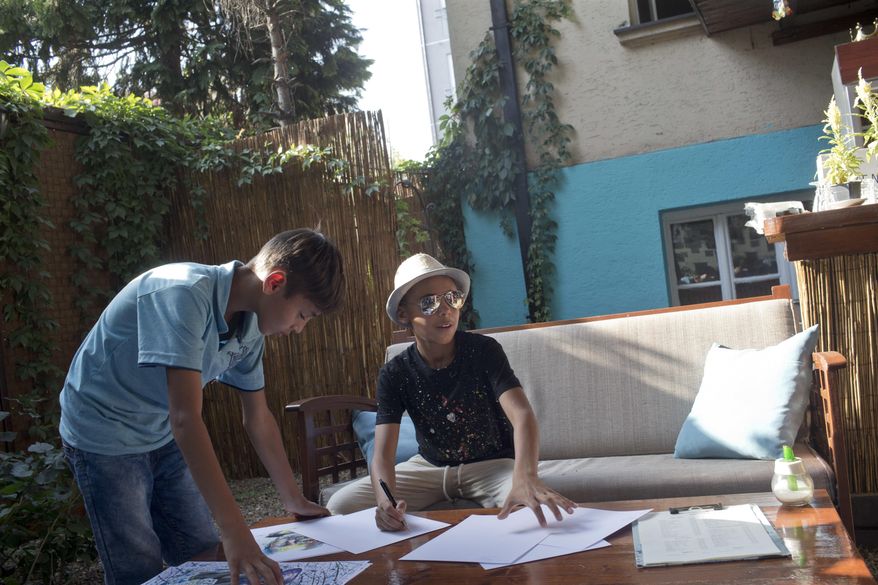 Farhad Nouri, center, signs copies of his work at an art exhibition in Belgrade, Serbia, Wednesday, Aug. 9, 2017. Nouri, a migrant boy from Afghanistan, has been nicknamed Little Picasso for artistic talent, and is using his first ever exhibition to help another little boy in need, a Serbian boy recovering from brain tumor surgery. (AP Photo/Marko Drobnjakovic)