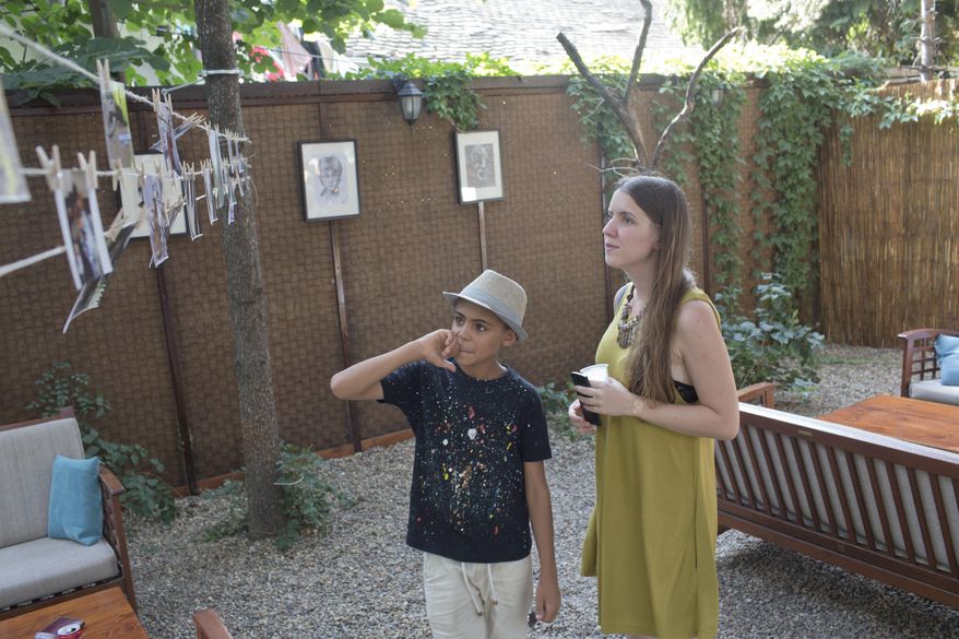 Farhad Nouri, center, observes his drawings on display at an art exhibition in Belgrade, Serbia, Wednesday, Aug. 9, 2017. Nouri, a migrant boy from Afghanistan, has been nicknamed Little Picasso for artistic talent, and is using his first ever exhibition to help another little boy in need, a Serbian boy recovering from brain tumor surgery. (AP Photo/Marko Drobnjakovic)