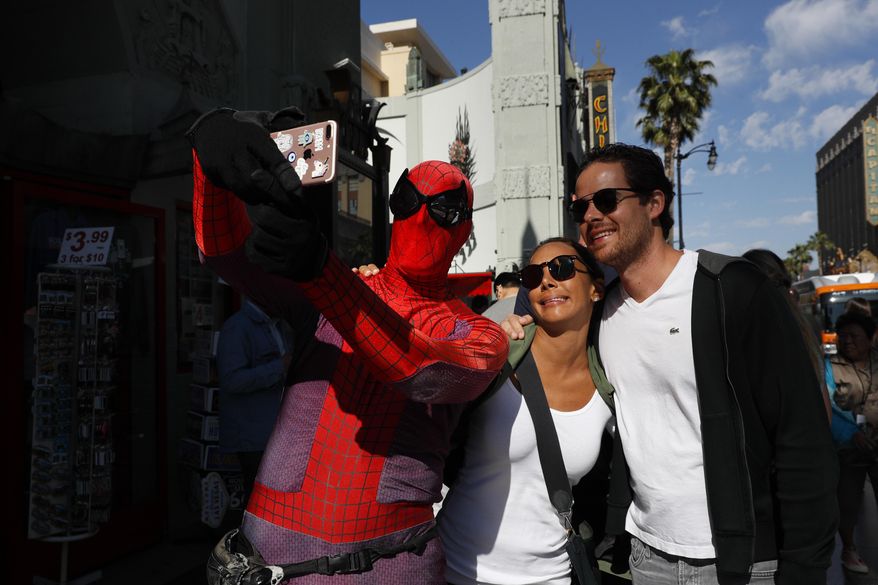 In this Wednesday, May 24, 2017 photo, superhero impersonator and actor Dan Inigo, left, uses a tourist's smartphone to take a selfie on Hollywood Boulevard in Los Angeles. "It's a place of diversity, it's a place of drama, it's a place of illusion … a place of broken dreams," says the 25-year-old actor who prowls the boulevard dressed as Spider-Man. Although he barely scrapes by, Inigo says it's still a great gig for a struggling actor who needs to keep a schedule open for auditions. (AP Photo/Jae C. Hong)