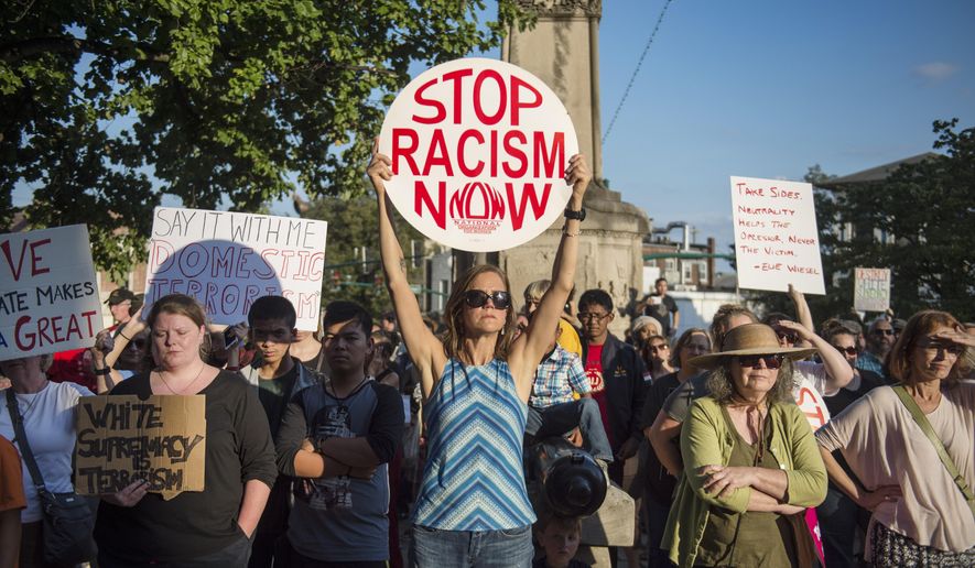 Cathi Crabtree, center, holds her "Stop Racism Now" sign high during a rally at the Monroe County Courthouse in Bloomington, Ind., Sunday, Aug. 13, 2017. Protesters decrying hatred and racism converged around the country Sunday, the day after a white supremacist rally that spiraled into violence in Charlottesville, Va. (Chris Howell/The Herald-Times via AP)