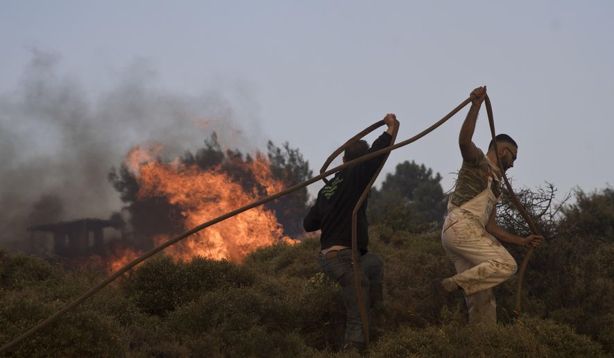 Volunteers try to extinguish the fire outside a military base at the village of Varnava , north of Athens, on Monday, Aug. 14, 2017. A large wildfire north of Athens is threatening homes as it sweeps through pine forest for a second day, uncontained due to high winds. (AP Photo/Petros Giannakouris)