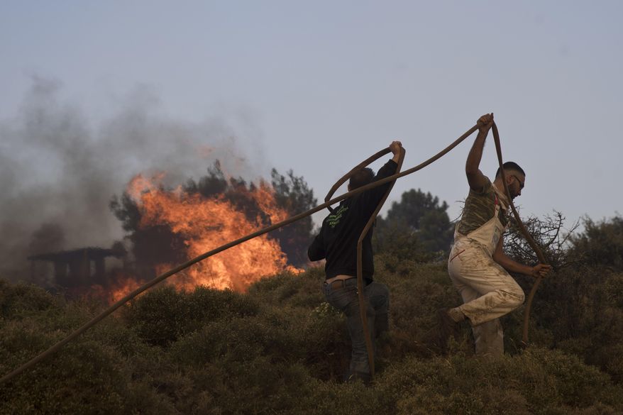 Volunteers try to extinguish the fire outside a military base at the village of Varnava , north of Athens, on Monday, Aug. 14, 2017. A large wildfire north of Athens is threatening homes as it sweeps through pine forest for a second day, uncontained due to high winds. (AP Photo/Petros Giannakouris)