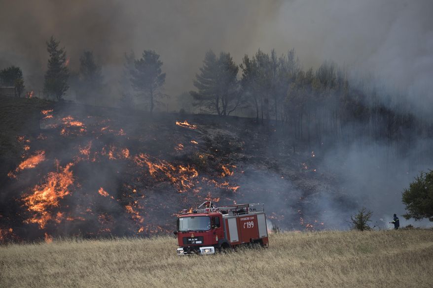 A firefighters sprays water during a forest fire in the village of Metohi north of Athens, on Monday, Aug. 14, 2017. A large wildfire north of Athens is threatening homes as it sweeps through pine forest for a second day, uncontained due to high winds.(AP Photo/Petros Giannakouris)
