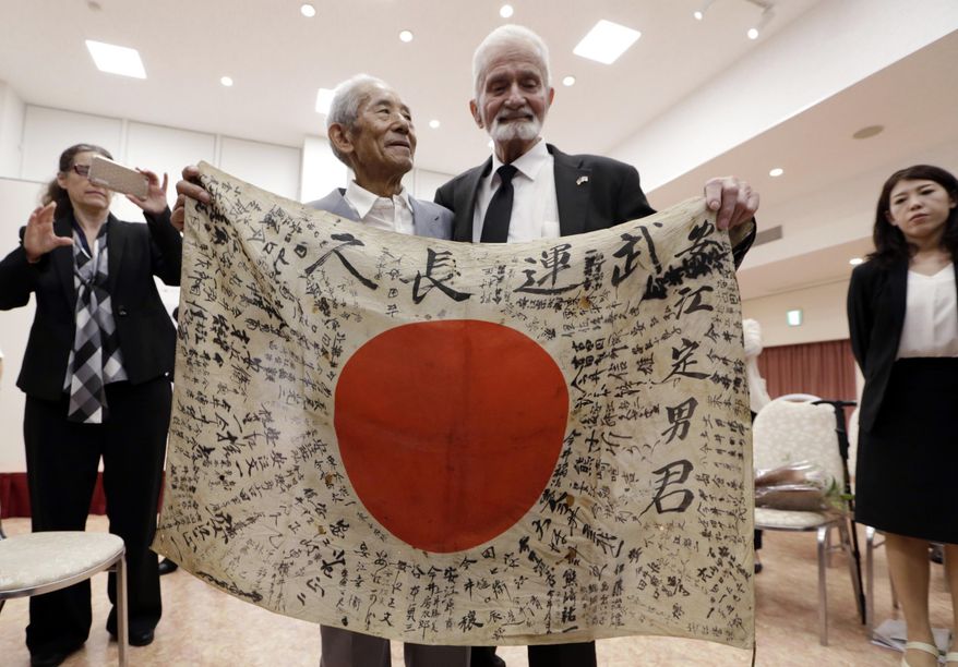 WWII veteran Marvin Strombo, right, and Tatsuya Yasue, 89-year-old farmer, hold a Japanese flag with autographed messages which was owned by his brother Sadao Yasue, who was killed in the Pacific during World Work II, during a ceremony in Higashishirakawa, in central Japan's Gifu prefecture Tuesday, Aug. 15, 2017. Strombo has returned to the fallen soldier's family the calligraphy-covered flag he took from the man's body 73 years ago. (AP Photo/Eugene Hoshiko)