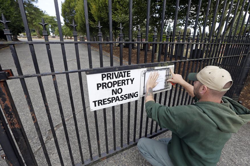 A worker, who declined to be identified, posts a notice of temporary closure on the locked gates of Lake View Cemetery, which was shut following angry messages they've received over a memorial for Confederate soldiers, Thursday, Aug. 17, 2017, in Seattle. The private cemetery was shut down a day earlier and is expected to remain closed through the weekend over a memorial that's stood there nearly a century and now there's a petition asking for it to come down. The memorial was built with help from the Daughters of the Confederacy 91 years ago. (AP Photo/Elaine Thompson)