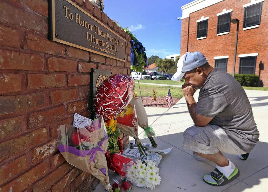 CORRECTS STATUS OF SECOND POLICE OFFICER - After placing flowers at a makeshift memorial, Miguel Velez, say's a prayer for the officer that was killed on Saturday, Aug. 19, 2017 in Kissimmee, Fla. The Kissimmee Police Department says Sgt. Sam Howard died Saturday from his injuries. His colleague, Officer Matthew Baxter, died Friday night after the attack in a neighborhood of Kissimmee, located south of the theme park hub of Orlando. (Red Huber/Orlando Sentinel via AP)