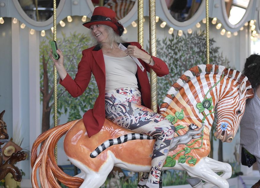 In this Tuesday, Aug. 15, 2017 photo, Nancy Hunter of Kings Valley, Ore., grabs a quick photo aboard Quigga a hand-carved Quagga while riding during the grand opening of Albany's Historic Carousel & Museum in Albany, Ore. (Mark Ylen/Albany Democrat-Herald via AP)