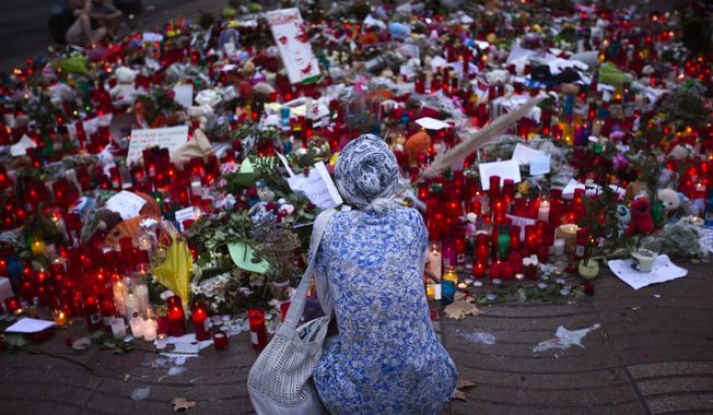 A woman sits next to candles and flowers placed on the ground after a terror attack that killed 14 people and wounded over 120 in Barcelona, Spain, Sunday, Aug. 20, 2017. (AP Photo/Emilio Morenatti)
