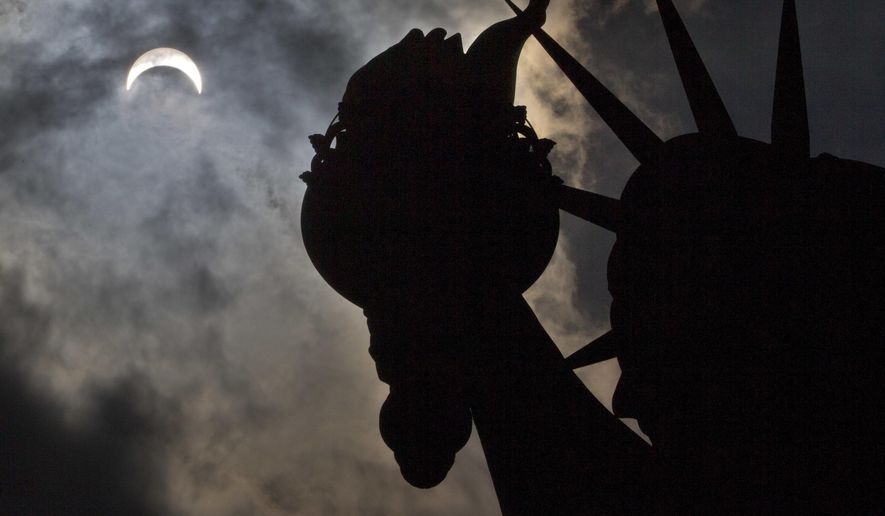 A partial solar eclipse appears over the Statue of Liberty on Liberty Island in New York, Monday, Aug. 21, 2017. (AP Photo/Seth Wenig)
