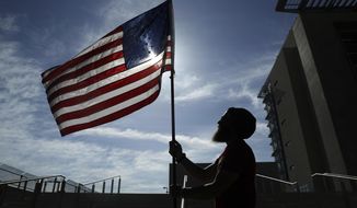 FILE - In this April 10, 2017 file photo, a protester holds up a flag outside of a federal courthouse in Las Vegas in support of defendants accused of wielding weapons against federal agents during a 2014 standoff involving cattleman and states&#39; rights advocate Cliven Bundy. A federal jury in Las Vegas is deliberating again Monday, Aug. 21, 2017, in the retrial of four men accused of wielding assault weapons against federal agents in a 2014 standoff near the Nevada ranch of anti-government figure Cliven Bundy. Jurors returned to work Monday, after spending a little more than two days last week going over five weeks of evidence in the case against four defendants. (AP Photo/John Locher, File)