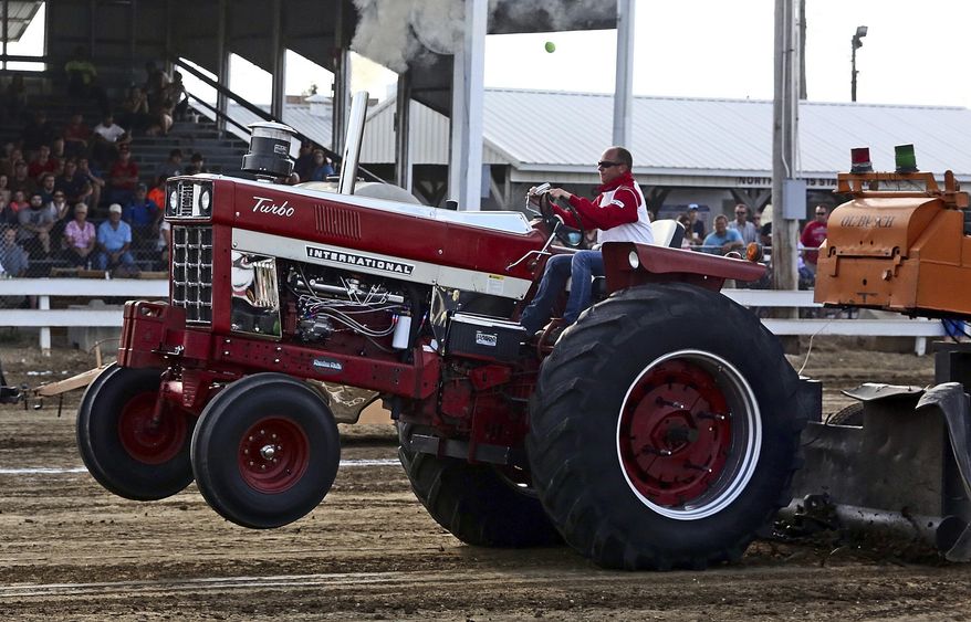 In this July, 31, 2017 photo, Ryan Kenady drives an International 1066 in the 11,500 lb. Farm Stock class at the Adams County Fair Tractor and Truck Pull in Mendon, Ill. Tractor pulling is not an inexpensive hobby. A decent 360 cubic-inch engine will cost $8,000 or more, and those giant back tires are $1,500 a pair. More than $10,000 will be needed get a good start, but one of the important keys to success revolves around the savvy and know-how of each individual operator. (Michael Kipley/The Quincy Herald-Whig via AP)
