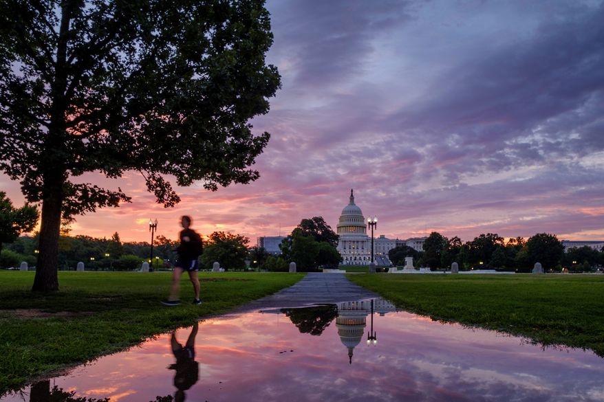 A pedestrian walks past a reflection of the U.S. Capitol in rain puddle at daybreak in Washington, Sunday, Aug. 13, 2017. (AP Photo/J. David Ake)