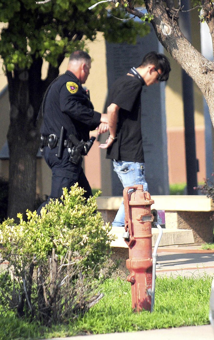 In this Monday, Aug. 28, 2017 photo, police take a man into custody after a shooting at a public library in the eastern New Mexico community of Clovis. Authorities on Tuesday identified the gunman accused of opening fire inside the library as a Nathaniel Jouett, 16-year-old high school student who they say killed a youth librarian and a second employee while wounding four others. The Associated Press generally does not identify juveniles accused of crimes, but is identifying Jouett because of the seriousness of the crime and because authorities said they plan to file a motion requesting the case's transfer from the juvenile system to adult court. (Tony Bullocks/Eastern New Mexico News via AP)