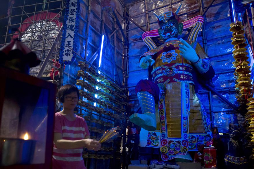 In this Sept. 2, 2017, photo, a woman burns joss sticks in front of a paper reproduction of the "Ghost King" at a makeshift altar during the "Hungry Ghost Festival" in Hong Kong. Countless hungry and restless ghosts are roaming Hong Kong, and the world, to visit their living ancestors, at least according to Chinese convention. In traditional Chinese belief, the seventh month of the lunar year is reserved for the Hungry Ghost festival, or Yu Lan, a raucous celebration marked by feasts and music. (AP Photo/Kin Cheung)