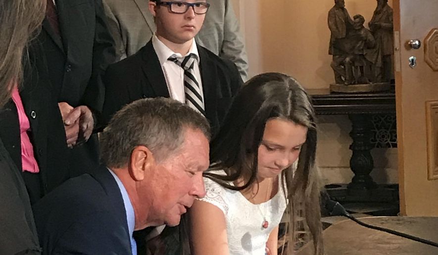 Madison Malinowski, 10, helps Ohio Gov. John Kasich sign "Judy's Law," named for her mother, at the Ohio Statehouse in Columbus, Ohio, Thursday, Sept. 7, 2017. Before her death, 33-year-old Judy Malinowski was hospitalized for nearly two years after her ex-boyfriend doused her with gasoline and set her on fire in August 2015. The law adds six years to prison terms for crimes that maim or disfigure victims. (AP Photo/Julie Carr Smyth)
