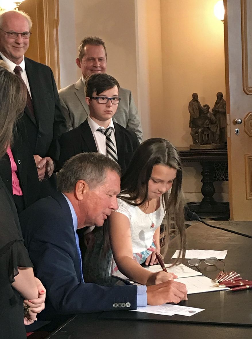 Madison Malinowski, 10, helps Ohio Gov. John Kasich sign "Judy's Law," named for her mother, at the Ohio Statehouse in Columbus, Ohio, Thursday, Sept. 7, 2017. Before her death, 33-year-old Judy Malinowski was hospitalized for nearly two years after her ex-boyfriend doused her with gasoline and set her on fire in August 2015. The law adds six years to prison terms for crimes that maim or disfigure victims. (AP Photo/Julie Carr Smyth)