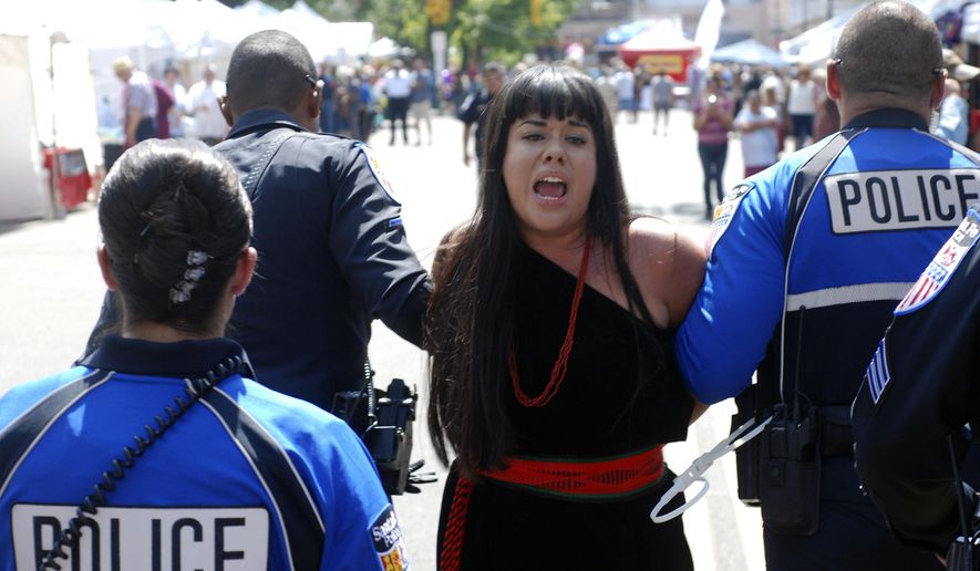 Police in Santa Fe, N.M., lead away protester organizer Jennifer Marley of San Ildefonso Pueblo in hand restraints on Friday, Sept. 8, 2017. Santa Fe police say they arrested at least 12 people to contain protest against an annual pageant marking the return of Spanish conquistador Don Diego de Vargas to New Mexico following a 17th century Indian revolt. Public statues and tributes to early Spanish conquerors are facing mounting criticism tied to the brutal treatment of American Indians centuries ago by Spanish soldiers and missionaries, with activists drawing ethical parallels to the national controversy over Confederate monuments. (AP Photo/Morgan Lee)