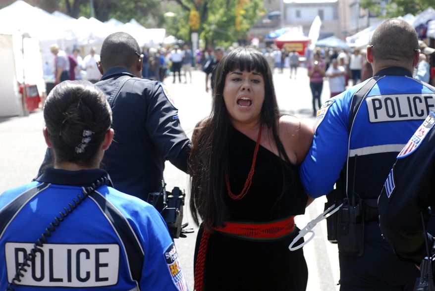 Police in Santa Fe, N.M., lead away protester organizer Jennifer Marley of San Ildefonso Pueblo in hand restraints on Friday, Sept. 8, 2017. Santa Fe police say they arrested at least 12 people to contain protest against an annual pageant marking the return of Spanish conquistador Don Diego de Vargas to New Mexico following a 17th century Indian revolt. Public statues and tributes to early Spanish conquerors are facing mounting criticism tied to the brutal treatment of American Indians centuries ago by Spanish soldiers and missionaries, with activists drawing ethical parallels to the national controversy over Confederate monuments. (AP Photo/Morgan Lee)