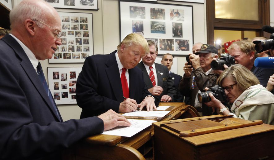 In this Nov. 4, 2015 photo, New Hampshire Secretary of State Bill Gardner watches, left, as Republican presidential candidate Donald Trump fills out his papers to be on the nation's earliest presidential primary ballot at The Secretary of State's office in Concord, N.H. Gardner said Friday, Sept. 8, 2017, that he will remain on the Presidential Advisory Commission on Election Integrity though he disagrees with voter fraud allegations made by the panel's vice chairman about his state.  (AP Photo/Jim Cole, File)
