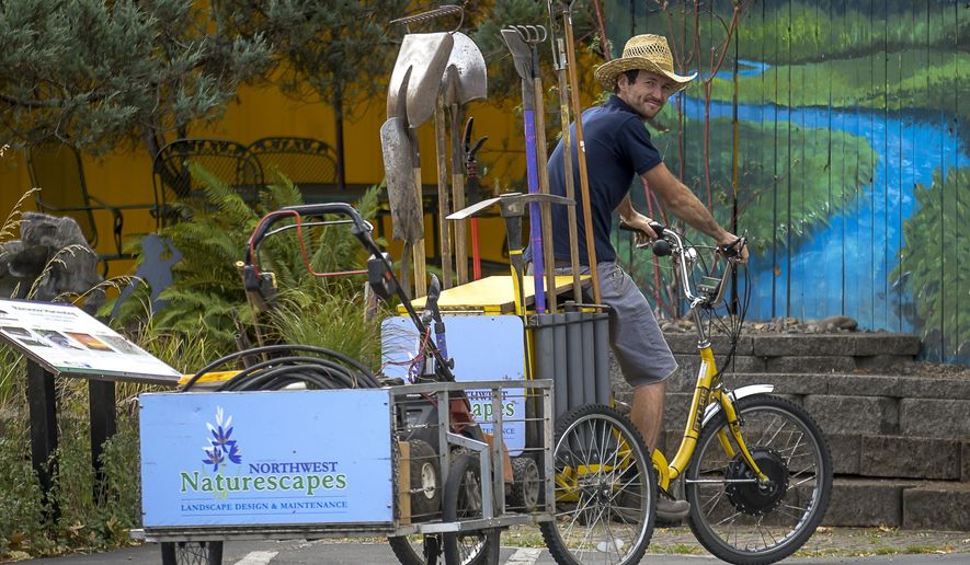 In this Aug. 30, 2017 photo, Alden Gray runs his landscaping business with the use of a three-wheeled bicycle poses at a client call at the First Alternative Co-op in Corvallis, Ore. (Andy Cripe/The Corvallis Gazette-Times via AP)