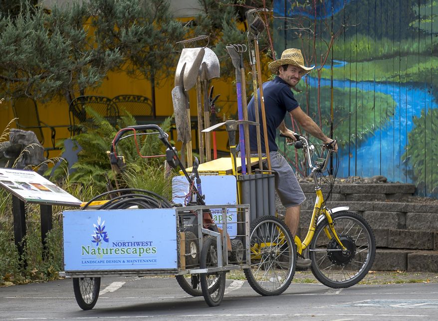 In this Aug. 30, 2017 photo, Alden Gray runs his landscaping business with the use of a three-wheeled bicycle poses at a client call at the First Alternative Co-op in Corvallis, Ore. (Andy Cripe/The Corvallis Gazette-Times via AP)