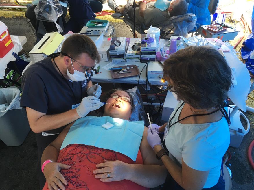 In this Friday, July 21, 2017, photo, dental student Carl Leiner, left, checks Lisa Kantsos teeth at the Remote Area Medical clinic in Wise, Va. Kantsos and hundreds of other uninsured patients came to the rural clinic for free dental and medical care. (AP Photo/Dylan Lovan)