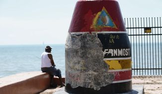 In this file photo, a man fishes next to the Southernmost Point Buoy damaged by Hurricane Irma, Wednesday, Sept. 13, 2017, in Key West of the Florida Keys. Police are searching for two people who burned a part of Key West&#39;s famous Southernmost Point buoy early New Year&#39;s Day 2022 after setting a fire near the landmark tourism icon. (AP Photo/Wilfredo Lee)  **FILE**