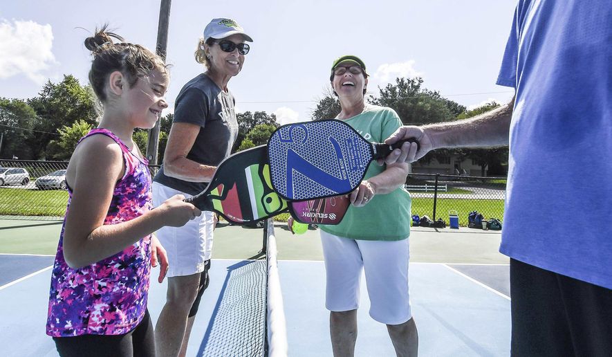 In this Aug. 12, 2017 photo, Natalie Alexander, left, celebrates with others after a game of pickle ball at Cresthaven Park in Decatur, Ill.Since Decatur Pickleball was founded in 2014, popularity of the sport has blossomed locally. While more than 100 people are associated with the group today. Created in the 1950s, the sport is a hybrid of tennis, badminton and pingpong that has become so popular in the United States, that it even has its own governing body, the United States of America Pickleball Association. (Clay Jackson/Herald & Review via AP)