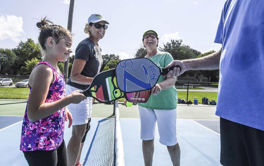 In this Aug. 12, 2017 photo, Natalie Alexander, left, celebrates with others after a game of pickle ball at Cresthaven Park in Decatur, Ill.Since Decatur Pickleball was founded in 2014, popularity of the sport has blossomed locally. While more than 100 people are associated with the group today. Created in the 1950s, the sport is a hybrid of tennis, badminton and pingpong that has become so popular in the United States, that it even has its own governing body, the United States of America Pickleball Association. (Clay Jackson/Herald & Review via AP)