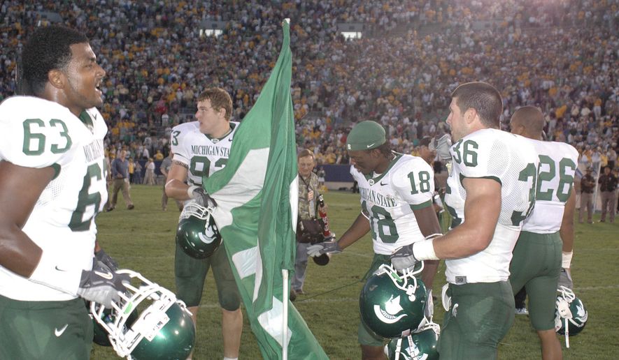 FILE - In this September 2005 file photo, Michigan State players Devin Pritchett (63), Nick Smith (93), Terry Love (18) and Eric Smith (36) plant a flag in the center of the field at Notre Dame Stadium following the team's 44-41 overtime victory in South Bend, Ind. Michigan State blew a 21-point before rallying. The victory spoiled the home debut of coach Charlie Weis and gave the Spartans five straight wins at Notre Dame Stadium, so few could blame them for celebrating at the Irish’s 50-yard line. But Notre Dame got its revenge a year later, outscoring Michigan State 19-0 in East Lansing in the fourth quarter for a 40-37 victory. (AP Photo/Joe Raymond, File)