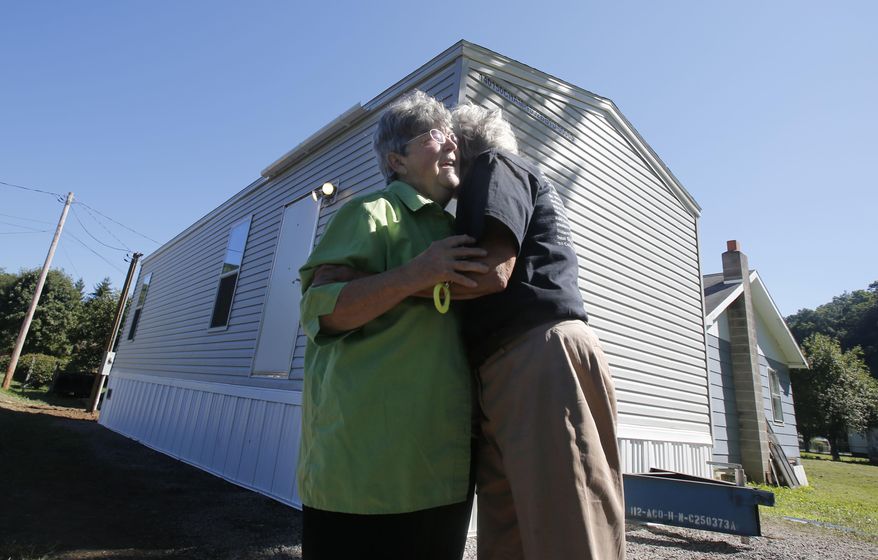 FILE - In this Aug. 23, 2016, file photo, Mayor Andrea "Andy" Pendleton, right, hugs resident Linda Bennett in front of Bennett's new FEMA trailer installed in front of her flood ravaged home in Rainelle, W. Va. Just before Hurricane Harvey made landfall in Texas in August 2017 as a Category 4 hurricane and in the floods that ensued, the federal government was auctioning off used disaster-response trailers at fire-sale prices. (AP Photo/Steve Helber, File)