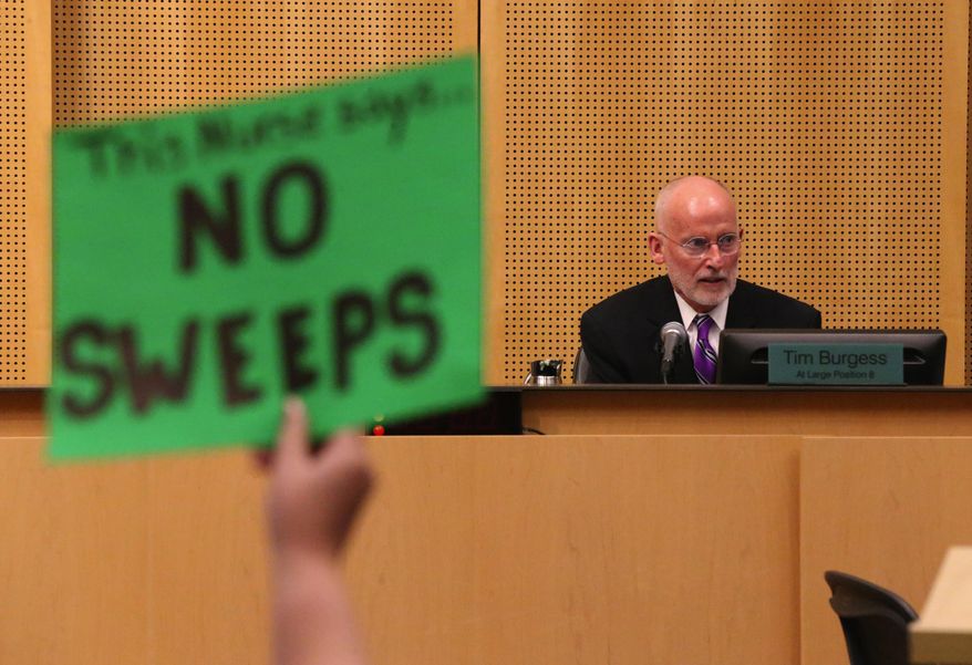 A protester holds up a sign against Seattle City Council member Tim Burgess, right, who has been chosen by the Seattle City Council as temporary mayor, Monday, Sept. 18, 2017, at City Hall in Seattle. (Ken Lambert/The Seattle Times via AP)