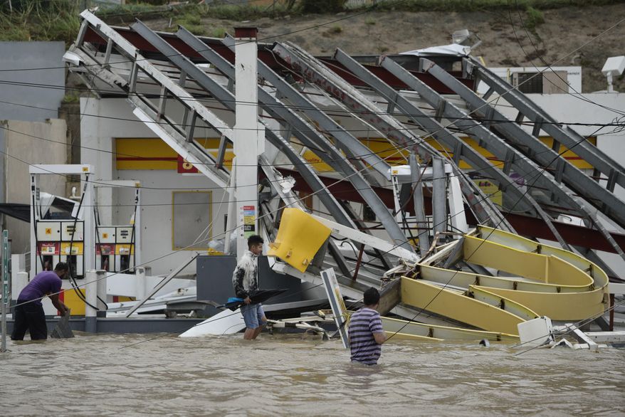 People walk next to a gas station flooded and damaged by the impact of Hurricane Maria, which hit the eastern region of the island, in Humacao, Puerto Rico, Wednesday, September 20, 2017. The strongest hurricane to hit Puerto Rico in more than 80 years destroyed hundreds of homes, knocked out power across the entire island and turned some streets into raging rivers in an onslaught that could plunge the U.S. territory deeper into financial crisis. (AP Photo/Carlos Giusti)