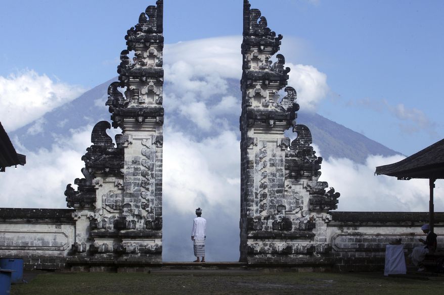 Balinese man watches Mount Agung volcano almost covered with clouds as he stands at a temple in Karangasem, Bali, Indonesia, Tuesday, Sept. 26, 2017. An increasing frequency of tremors from the volcano indicates magma is continuing to move toward the surface and an eruption is possible, a disaster agency official said Tuesday. Tourists are cutting short their stay to the island, where an eruption would force the airport to close and strand thousands. (AP Photo/Firdia Lisnawati)