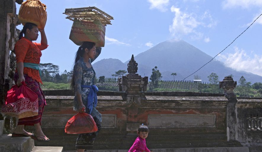 Women carry offerings at a temple about 10 kilometers (6.3 miles) from Mount Agung volcano, rear, at Pemuteran village in Karangasem, Bali, Indonesia, Wednesday, Sept. 27, 2017. Warnings that a volcano on the Indonesian tourist island of Bali will erupt have sparked an exodus of more than 75,000 people that is likely to continue to swell, the country&#39;s disaster agency said. (AP Photo/Firdia Lisnawati)