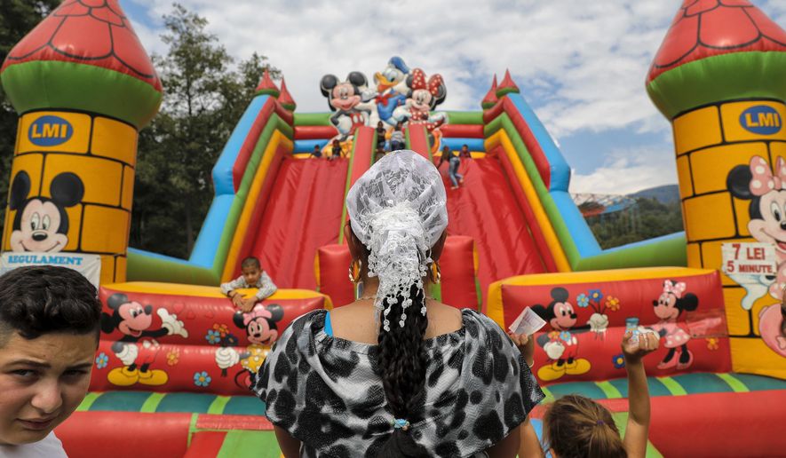 In this Friday, Sept. 8, 2017 photograph, a Roma woman watches children play in Costesti, Romania. Hundreds of Gypsies or Roma got on their knees and kissed the relics of Orthodox St. Gregory, at the hillside 15th-century monastery in southern Romania, for their annual celebration of the birthday of St. Mary, the mother of Jesus.(AP Photo/Vadim Ghirda)