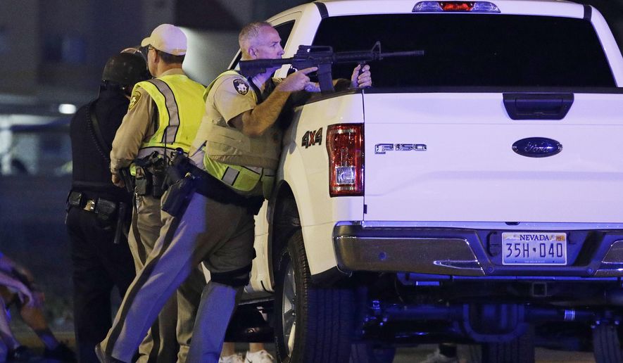 A police officer takes cover behind a truck at the scene of a shooting near the Mandalay Bay resort and casino on the Las Vegas Strip, Sunday, Oct. 1, 2017, in Las Vegas. Multiple victims were being transported to hospitals after a shooting late Sunday at a music festival on the Las Vegas Strip. (AP Photo/John Locher)