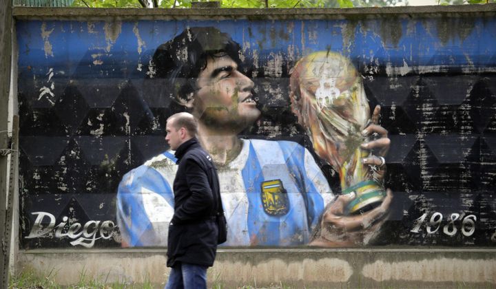 A man walks past a fence with graffiti depicting Argentina&#x27;s soccer legend Diego Maradona in the town of Volkhov, 130 km (80 miles) east of St.Petersburg, Russia, Monday, Oct. 2, 2017. (AP Photo/Dmitri Lovetsky)