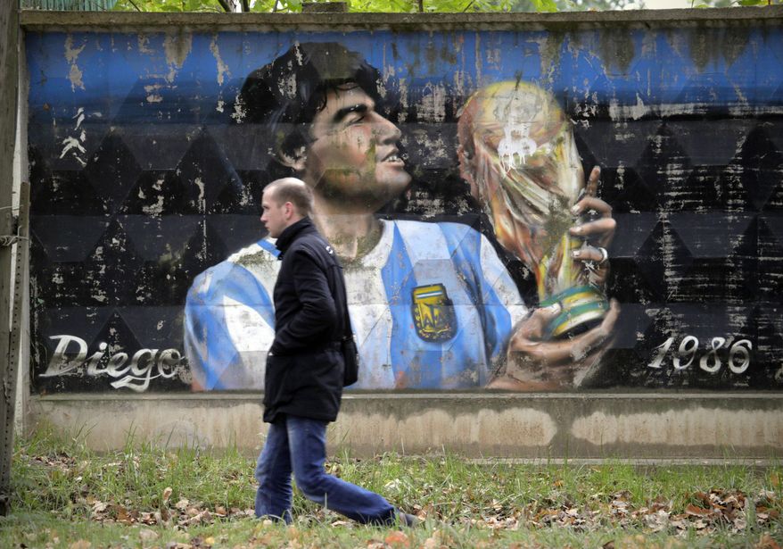 A man walks past a fence with graffiti depicting Argentina's soccer legend Diego Maradona in the town of Volkhov, 130 km (80 miles) east of St.Petersburg, Russia, Monday, Oct. 2, 2017. (AP Photo/Dmitri Lovetsky)