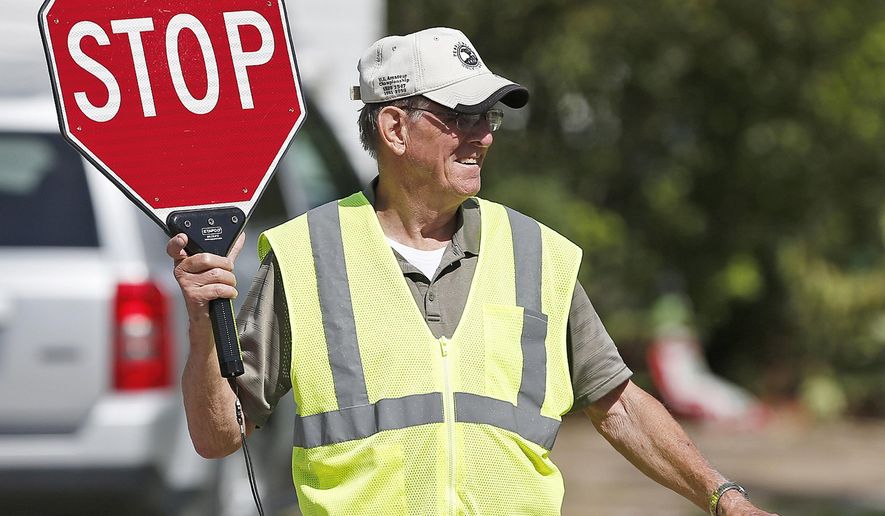 In this Sept. 9, 2017 file photo, George Caspermeyer smiles while directing traffic as a crossing guard for Madison School students in Quincy, Ill. Caspermeyer has worked the corner for the last 19 years and plans to not work when the school closes. The retired-Moorman Manufacturing fork lift driver and longtime guard that has guided kids to safety across the street as they walk home will step down when Madison closes next year. With the transitioning of students into a new buildings, there will be less demand for crossing guards. (Jake Shane /The Quincy Herald-Whig via AP)