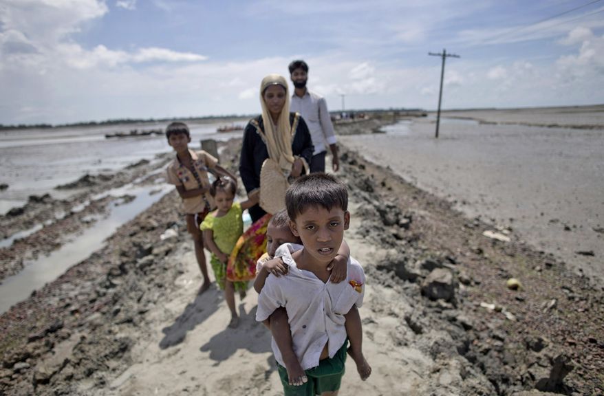 In this Oct. 2, 2017 photo, newly arrived Rohingya refugee Yosar Hossein, 7, carries his baby sister Noyem Fatima and walks followed by his other siblings and mother Firoza Begum on a mud bank leading to a Bangladesh army run processing center where they will be allotted their camp, in Teknaf, Bangladesh. Barefoot and still wearing his school uniform, the 7-year-old is among more than a half million persecuted Rohingya Muslims fleeing neighboring Myanmar. (AP Photo/Gemunu Amarasinghe)