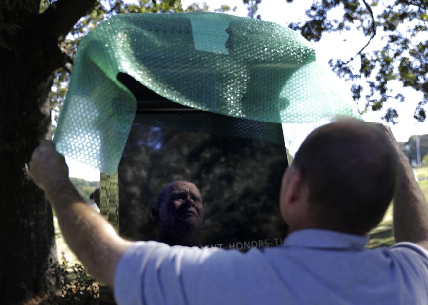 In this Friday, Oct. 20, 2017 photo, a monument to honor African-Americans who were buried in unmarked graves in the previously segregated Alta Vista Cemetery is wrapped by cemetery superintendent Tommy Casper after being displayed for a photo in Gainesville, Ga. The previously unmarked graves of more than 1,100 black souls buried in the cemetery will be honored with a memorial to be dedicated Sunday. Recently, the city discovered the extent of the unmarked graves using ground-penetrating radar. (AP Photo/David Goldman)