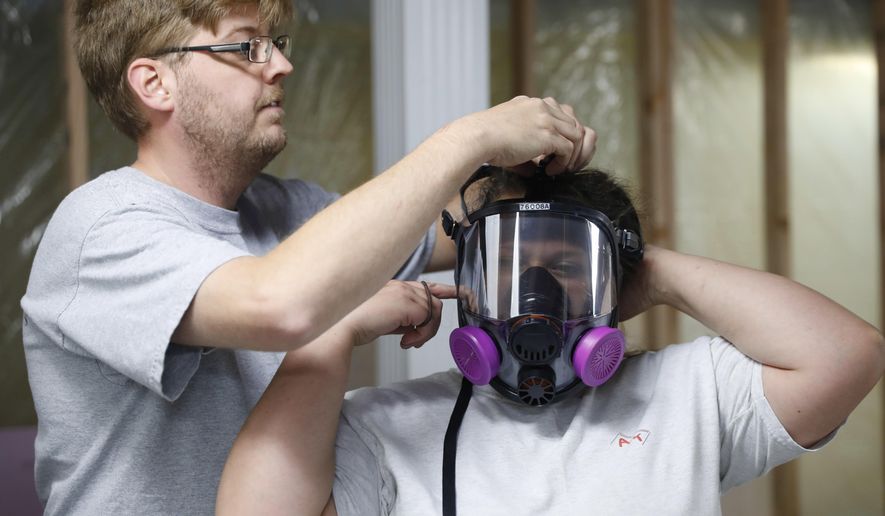 In this July 12, 2017, photo, Asbestos Removal Technologies Inc., job superintendent Ryan Laitila, helps forman Megan Eberhart adjust a HEPA high efficiency particulate respirator mask for asbestos abatement in Howell, Mich. Asbestos fibers can become deadly when disturbed in a fire or during remodeling, lodging in the lungs and causing problems including mesothelioma, a form of cancer. The material’s dangers have long been recognized. But a 1989 attempt to ban most asbestos products was overturned by a federal court, and it remains in widespread use. (AP Photo/Paul Sancya)