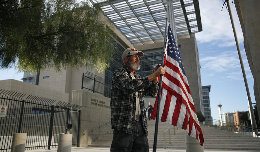 Supporter David Fleeman hangs a flag outside of the federal courthouse, Monday, Oct. 30, 2017, in Las Vegas. Jury selection is set to begin in Las Vegas for the long-awaited trial of Nevada cattleman and states' rights figure Cliven Bundy, two sons and one other co-defendant on charges stemming from an armed standoff with federal agents in April 2014. (AP Photo/John Locher)