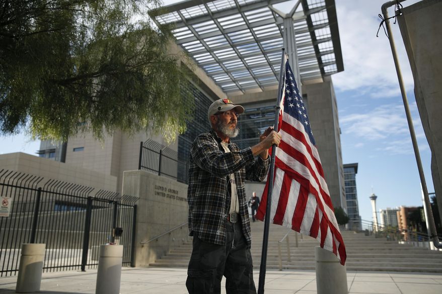 Supporter David Fleeman hangs a flag outside of the federal courthouse, Monday, Oct. 30, 2017, in Las Vegas. Jury selection is set to begin in Las Vegas for the long-awaited trial of Nevada cattleman and states' rights figure Cliven Bundy, two sons and one other co-defendant on charges stemming from an armed standoff with federal agents in April 2014. (AP Photo/John Locher)